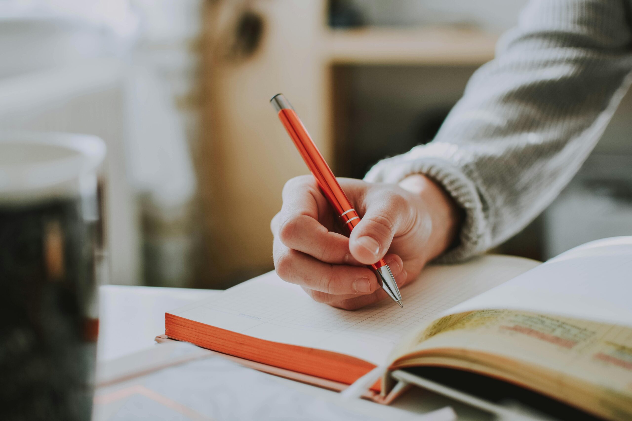 A woman writing in a notebook with an orange pen